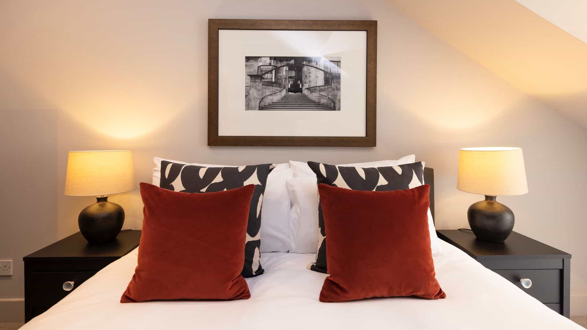 Neatly stacked pillows on a bed with white linen, black bedside cabinets and lamps